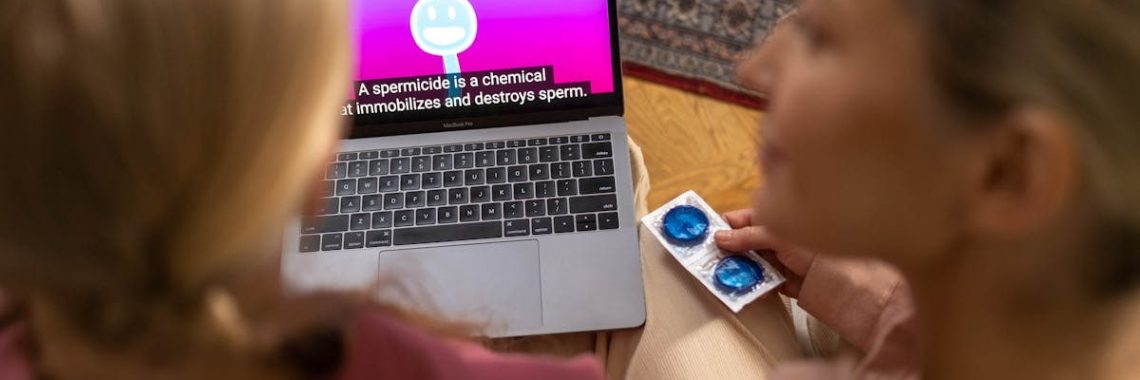 Two women watching an educational video on contraception and holding condoms indoors.