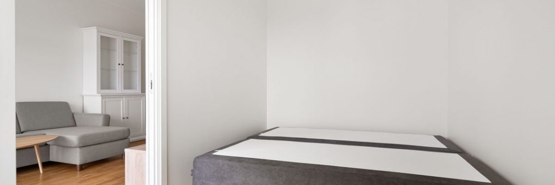 Spacious minimalist bedroom featuring a modern sofa and bed frame with wooden parquet flooring.